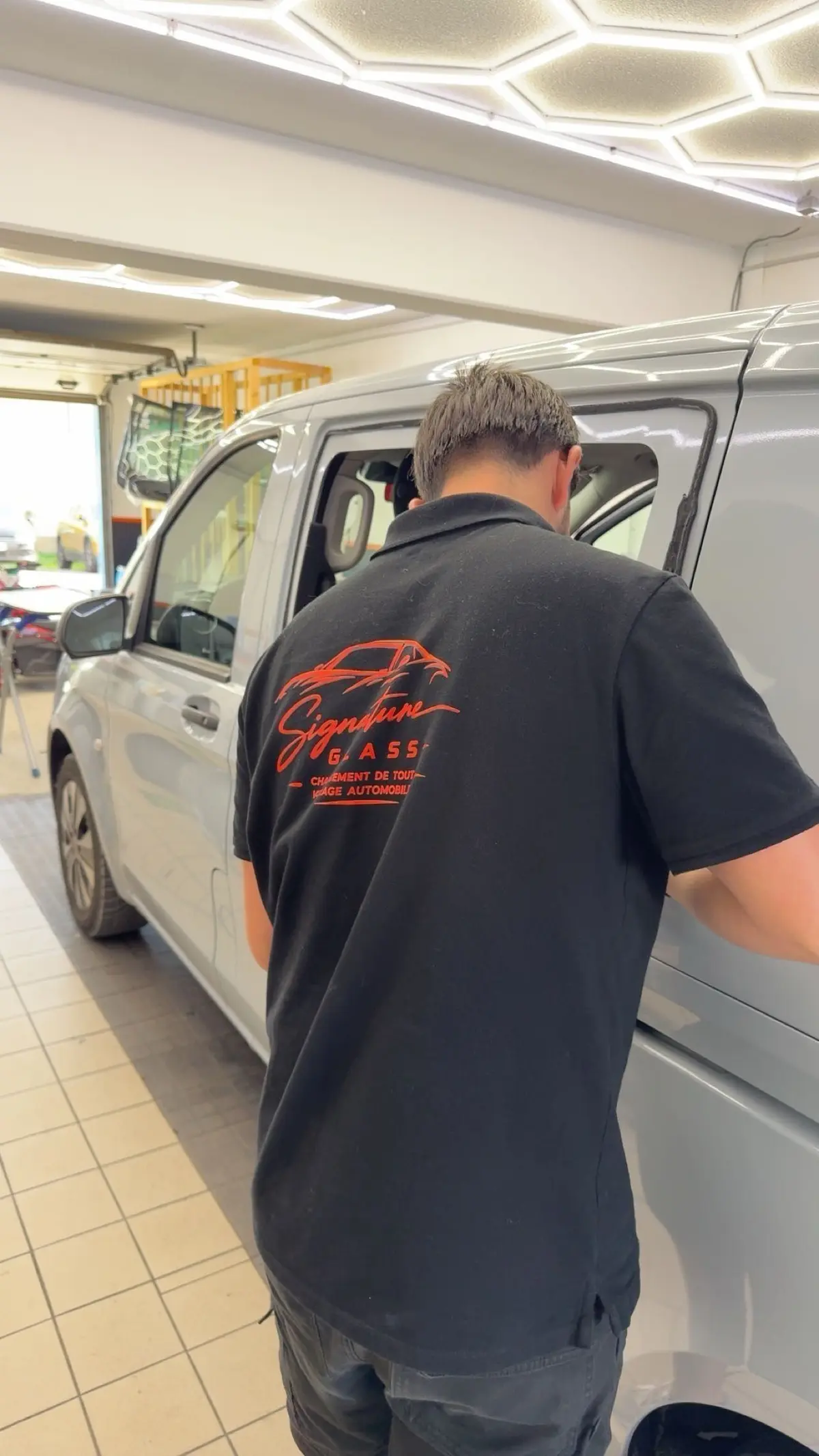 Technicien Signature Glass en polo de l'entreprise, en intervention sur la porte d'un utilitaire blanc